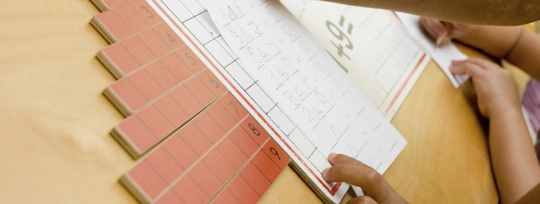 Manos trabajando con material Montessori de números y una guía de trabajo